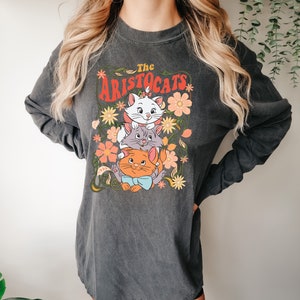 May include: Dark gray long-sleeve shirt featuring a graphic of three cartoon cats from "The Aristocats" movie, surrounded by flowers. The text "The Aristocats" is in a retro font. The shirt has a vintage, washed look.