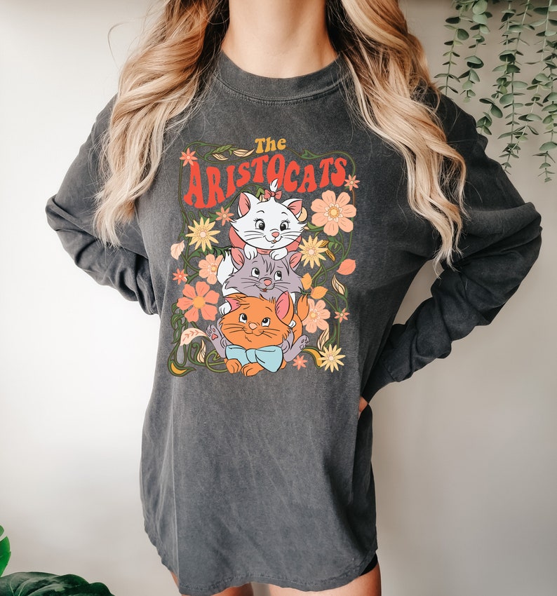 May include: Dark gray long-sleeve shirt featuring a graphic of three cartoon cats from "The Aristocats" movie, surrounded by flowers. The text "The Aristocats" is in a retro font. The shirt has a vintage, washed look.