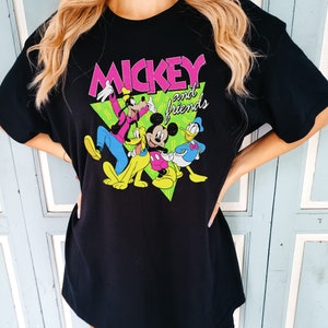 May include: Black t-shirt with a colourful graphic of Mickey Mouse and friends. The design features Mickey, Donald Duck, Goofy, and Pluto, with the words "Mickey and friends" in pink and white. The characters are set against a green triangle.