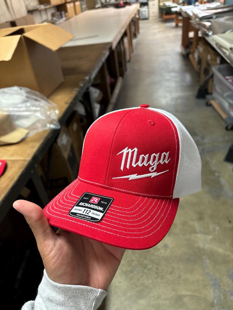 May include: Red and white trucker hat with a white embroidered lightning bolt and the word "Maga" on the front. The hat is made by Richardson 112.