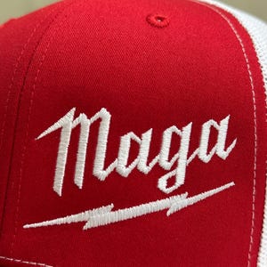 May include: A red and white trucker hat with a white embroidered logo that says "Maga" with a lightning bolt underneath.