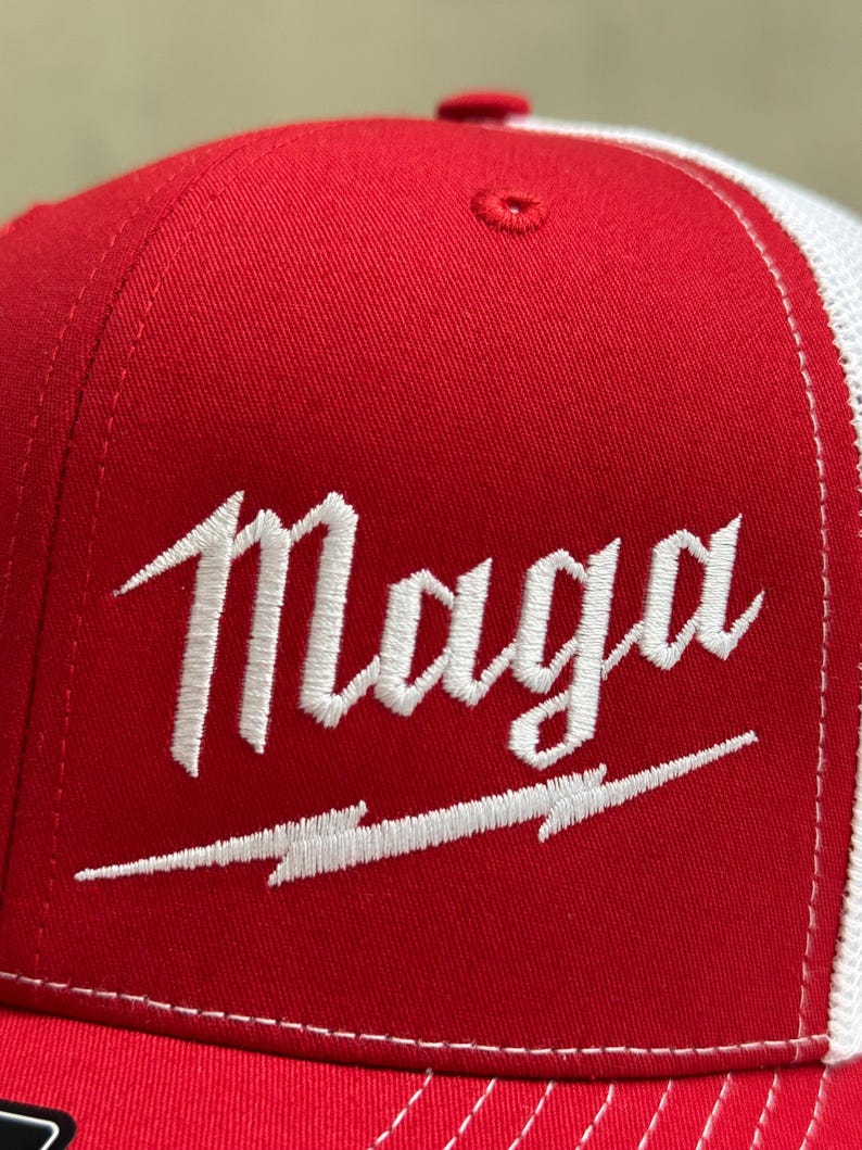 May include: A red and white trucker hat with a white embroidered logo that says "Maga" with a lightning bolt underneath.