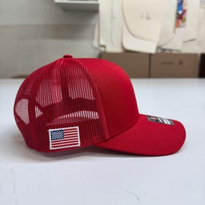 May include: A red mesh trucker hat with a small American flag patch on the side.