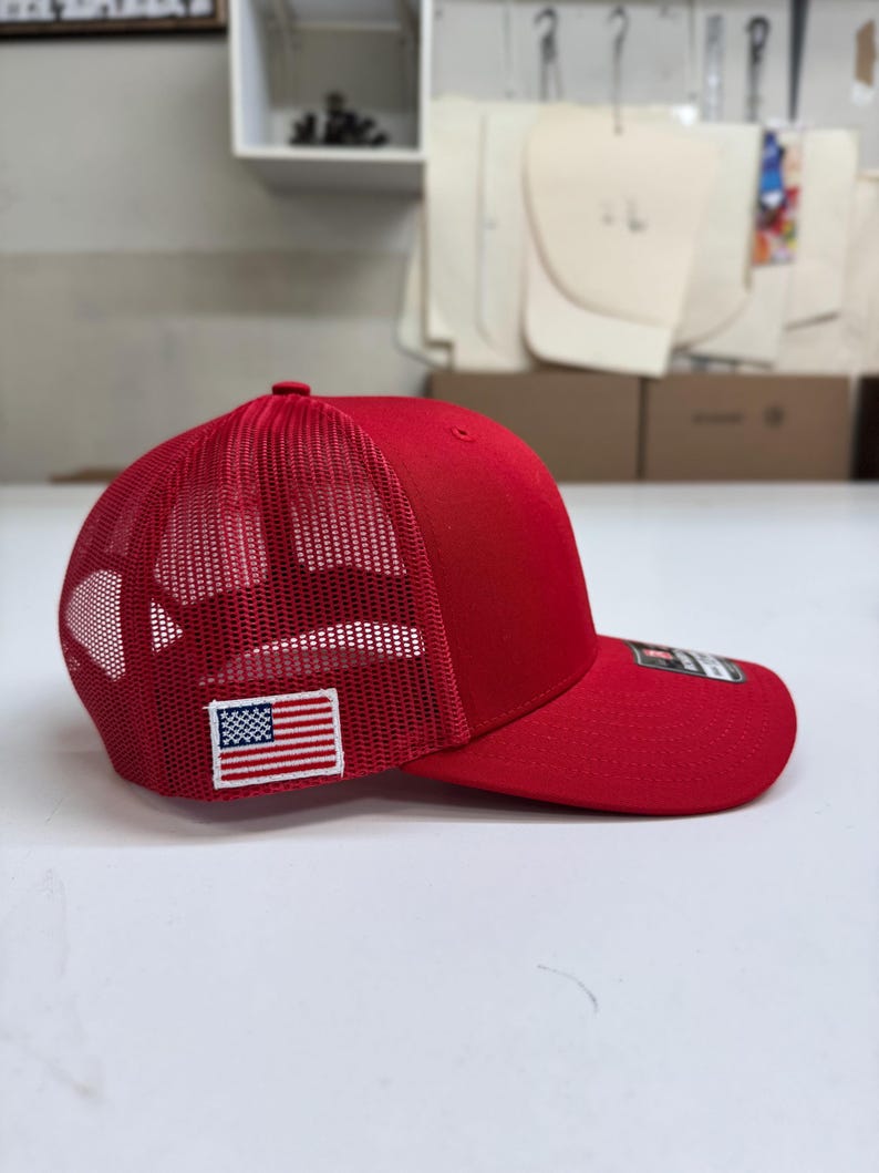 May include: A red mesh trucker hat with a small American flag patch on the side.
