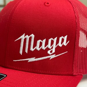May include: Red and black trucker hat with a white embroidered logo that says "Maga" with a lightning bolt underneath.