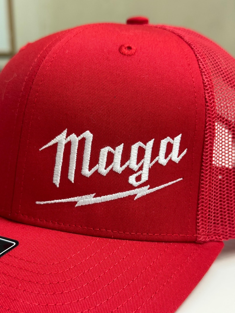 May include: Red and black trucker hat with a white embroidered logo that says "Maga" with a lightning bolt underneath.