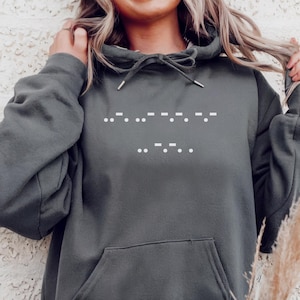 May include: A dark grey hooded sweatshirt with a drawstring and a front pocket. The sweatshirt displays white dots and dashes in Morse code across the chest. The Morse code spells out the word "Sorry".