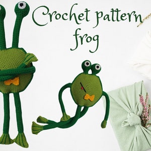 May include: Crochet pattern for a frog. Two green crocheted frogs with long legs and big eyes are shown on a white background. The larger frog has its arms crossed over its chest. The smaller frog has its arms outstretched. The text "Crochet pattern frog" is written in green cursive above the frogs.