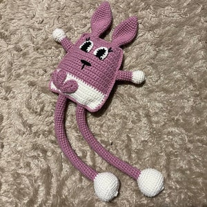May include: A pink crocheted bunny with long legs and white feet. The bunny has large black eyes and a white nose.