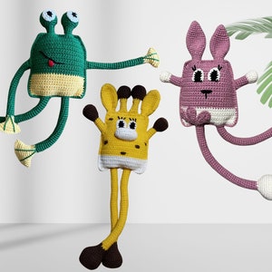May include: Three handmade crochet stuffed animals: a green frog, a yellow giraffe, and a pink bunny. Each has long limbs and a whimsical design. The frog has large eyes and a red tongue. The giraffe has brown spots. The bunny has long ears.