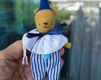 May include: A handmade teddy bear doll dressed in a blue and white striped outfit, a white collar, and a blue hat with a pom-pom. The bear has a tan body and is holding a blue bow.