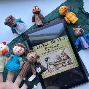 Pu&ograve; includere: Una collezione di marionette a dito fatte a mano, tra cui un orso, un gufo, un'anatra e una bambina, disposte attorno a un tablet che mostra la copertina del libro "Little Bear's Friend". Le marionette sono di vari colori, con illustrazioni sulla copertina.