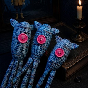Op de afbeelding: Drie blauwe gehaakte wezens met roze knoopogen en meerdere tentakels. Ze zijn gerangschikt op een donker oppervlak met een boek en een brandende kaars op de achtergrond. De afbeelding heeft een grillige, handgemaakte uitstraling.