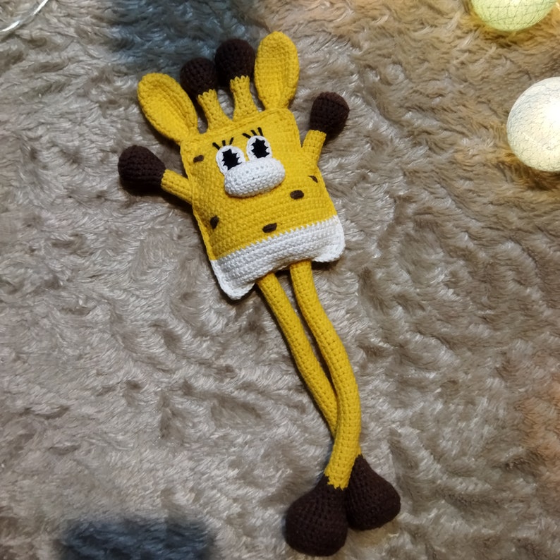 May include: A crocheted giraffe toy with long legs and a yellow and white body. The giraffe has brown eyes and a brown nose.