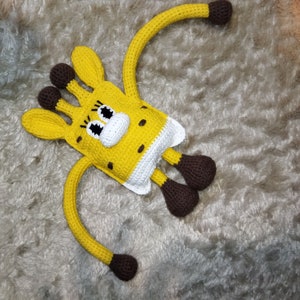 May include: A crocheted giraffe toy with brown legs and yellow and white body. The giraffe has large, black eyes and a white nose.