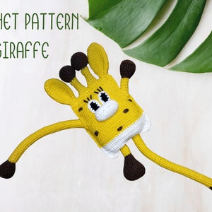 以下が含まれることがあります： 茶色の斑点、耳、足が付いた黄色の手編みのキリンのおもちゃ。キリンは白と黒の顔をしています。「CROCHET PATTERN GIRAFFE」というテキストは緑色です。おもちゃは、大きな緑の葉が付いた白い背景にあります。
