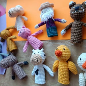 May include: A collection of handmade crochet animal dolls, including a bear, pig, cow, duck, and others. The dolls are in various colors, such as brown, pink, yellow, and white. Each doll has unique features and details.