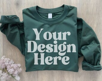 May include: A dark green long-sleeved t-shirt with the text "Your Design Here" printed in white on the front.