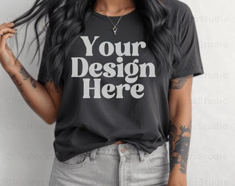 May include: A black t-shirt with the text "Your Design Here" in white. The shirt is being worn by a person with long black hair and tattoos on their arms. The person is wearing light gray denim shorts.