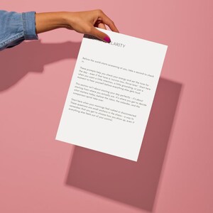 Op de afbeelding: Een wit papier met de titel "Morning Clarity" wordt door een hand vastgehouden tegen een roze achtergrond. Het papier bevat tekst over het stellen van intenties en het controleren van energie. De tekst is zwart.