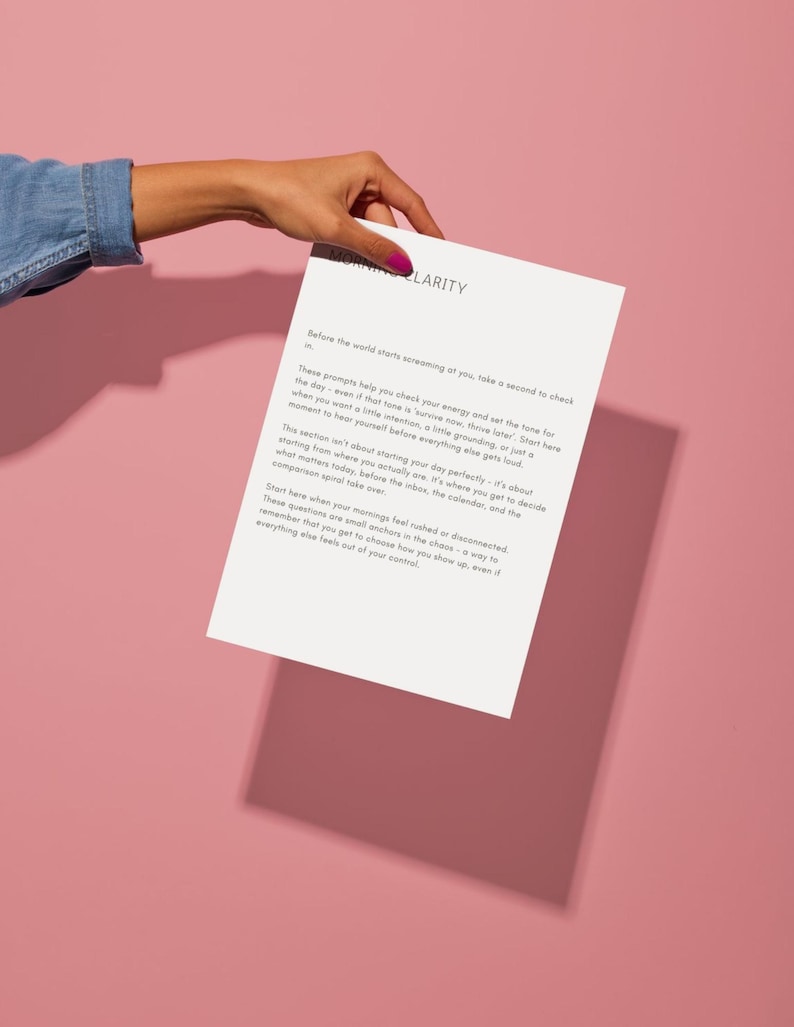 Op de afbeelding: Een wit papier met de titel "Morning Clarity" wordt door een hand vastgehouden tegen een roze achtergrond. Het papier bevat tekst over het stellen van intenties en het controleren van energie. De tekst is zwart.