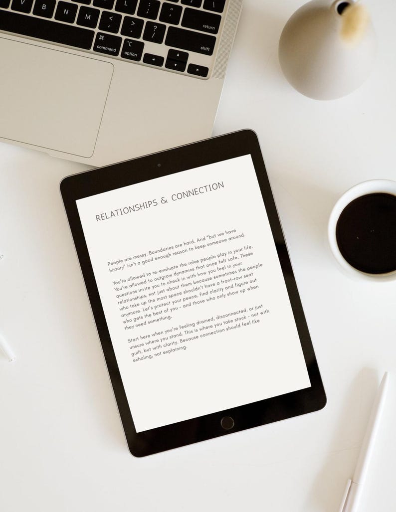 Op de afbeelding: Een zwarte tablet met tekst over relaties en verbinding, samen met een laptop, een koffiekopje en een decoratieve vaas op een wit oppervlak. De tekst op de tablet luidt "RELATIONSHIPS & CONNECTION". Een pen is ook zichtbaar.