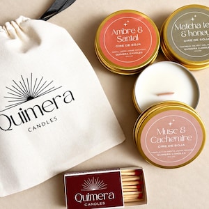 Könnte beinhalten: Ein cremefarbener Beutel mit Kordelzug und dem Quimera Candles Logo, drei runde goldfarbene Dosen mit Sojawachskerzen mit den Aufschriften Ambre & Santal, Matcha tea & honey und Musc & Cachemire sowie eine kleine Schachtel mit Streichhölzern.
