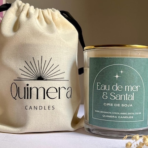 May include: A candle in a glass jar with a gold rim, labelled "Eau de mer & Santal" and "Cire de Soja." Beside it is a cream drawstring bag with the "Quimera Candles" logo. The candle is a soy wax candle.