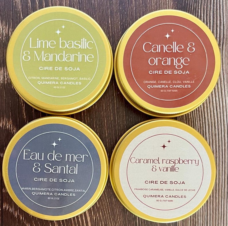 May include: Four round, gold-rimmed soy wax candles in tins. The labels feature text in French, including "Lime basilic & Mandarine," "Canelle & orange," "Eau de mer & Santal," and "Caramel, raspberry & vanille." Each tin is 60g / 2 oz.