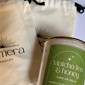 May include: A candle in a clear glass jar with a gold rim and a green label reading "Matcha tea & honey". Two off-white drawstring bags with the "Quimera Candles" logo are visible.