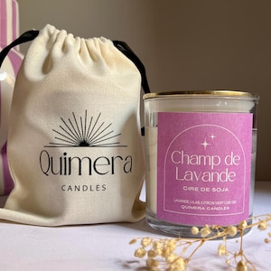 May include: A clear glass candle with a gold rim and a purple label that reads "Champ de Lavande". A beige drawstring bag with the "Quimera Candles" logo is next to the candle. The candle is labeled "Cire de Soja".