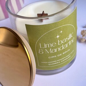 May include: A clear glass candle jar with a gold lid, featuring a white wax candle with a wooden star-shaped wick. The label reads "Lime Basilic & Mandarine, Cire de Soja, Quimera Candles."
