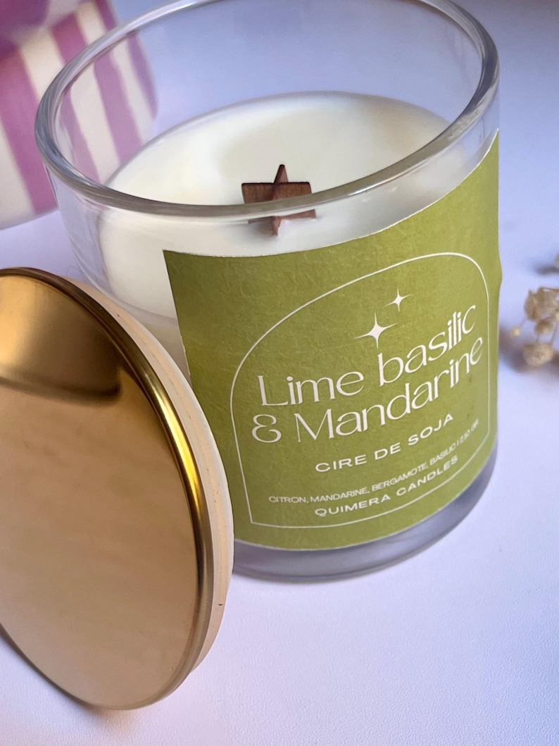 May include: A clear glass candle jar with a gold lid, featuring a white wax candle with a wooden star-shaped wick. The label reads "Lime Basilic & Mandarine, Cire de Soja, Quimera Candles."