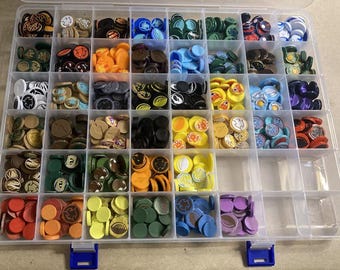 May include: A clear plastic storage box with multiple compartments filled with colorful game pieces. The pieces are round and have various designs and colors, including red, blue, green, yellow, and brown.