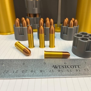 May include: A close-up of a ruler with the word "WESTCOTT" printed on it.  There are several gold-colored bullets on a white surface.  The bullets are arranged in a row and are about 5 cm long.
