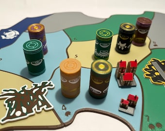 May include: A board game with a map design, featuring cylindrical game pieces in various colors like green, brown, and purple. Small red-roofed building miniatures and abstract tokens are also present.