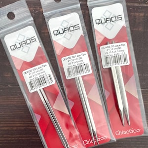May include: Three packages of QUADS SS Lace Tips knitting needles. The packages are clear plastic with red and white accents. The needles are silver and measure 4 inches (10 cm). The packages have the brand name and size information printed on them.