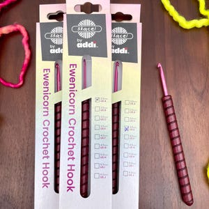 May include: Three sets of purple and black Ewenicorn crochet hooks in various sizes, packaged in white boxes with the brand name "skacel by addi" printed on them.