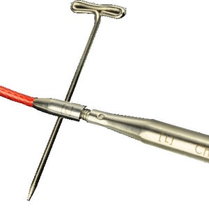 Peut inclure: Une aiguille à tricoter en argent avec un cordon rouge attaché à l'extrémité. L'aiguille est étiquetée "ChiaoGoo 10.5 (6.5mm)".