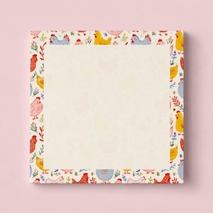 May include: Square notepad with a cream-colored center and a border featuring colorful chickens and floral designs. The chickens are in various colors, including red, yellow, and blue. The notepad is on a light pink background.