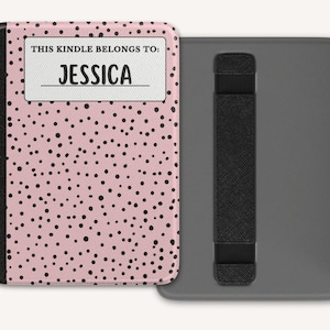 Könnte beinhalten: Eine rosa Kindle-Hülle mit schwarzen Tupfen und dem Text "THIS KINDLE BELONGS TO: JESSICA" in einem weißen Rechteck. Die Hülle ist geöffnet und zeigt eine graue Rückseite mit einem schwarzen Handriemen.