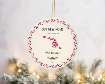 Puede incluir: Adorno navideño redondo de cerámica con el texto "OUR NEW HOME" y "Ann Arbor, MI". El adorno presenta un borde de bastón de caramelo rojo y blanco, un contorno rojo del estado de Michigan y el texto "The Whites" y "2024".