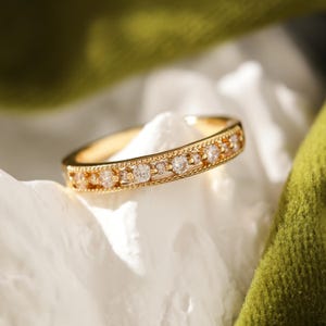 May include: A gold band ring with a row of small, clear gemstones set in a delicate, ornate design.
