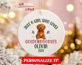 May include: A white, round Christmas ornament with a golden cord for hanging. The ornament features a brown Goldendoodle illustration and the text "JUST A GIRL WHO LOVES GOLDENDOODLES OLIVIA 2025". Decorative elements include snowflakes and holly.