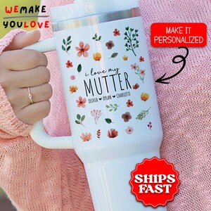 May include: White insulated tumbler with floral designs and the text "i love my MUTTER" with names below. The tumbler has a white handle and a silver rim. The image also includes the text "WE MAKE YOU LOVE", "MAKE IT PERSONALIZED", and "SHIPS FAST".