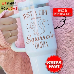 May include: White insulated tumbler with a handle, featuring a squirrel illustration and the text "JUST A GIRL who loves Squirrels OLIVIA". The tumbler has a silver rim and a white lid. A red sticker says "MAKE IT PERSONALIZED".