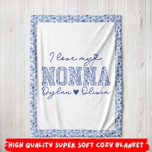May include: White blanket with a blue floral border and the text "I love my NONNA Dylan Olivia" in blue. The blanket has a soft, cozy appearance, perfect for gifting.