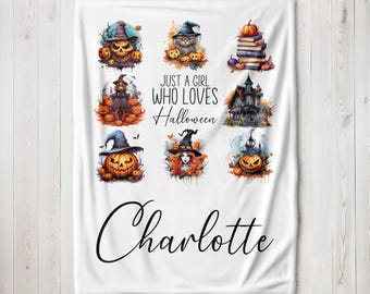 May include: White fleece blanket with a Halloween theme. It features a variety of illustrations including pumpkins, witches, cats, and a haunted house. The text reads "Just a girl who loves Halloween" and "Charlotte".