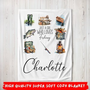 Puede incluir: Una manta de franela blanca con un tema de pesca. Presenta una caña de pescar, un cubo de pescado, una linterna, una caja de aparejos y un par de botas. El texto dice "Just a girl who loves fishing" y "Charlotte".
