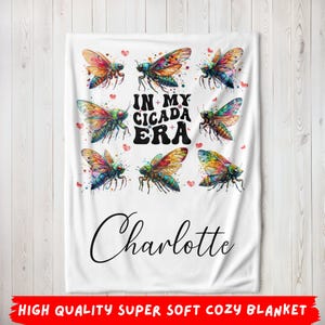 May include: White blanket featuring colorful cicada illustrations and the text "IN MY CICADA ERA". The blanket also includes the name "Charlotte" in a script font. Small red hearts are scattered around the cicada images.